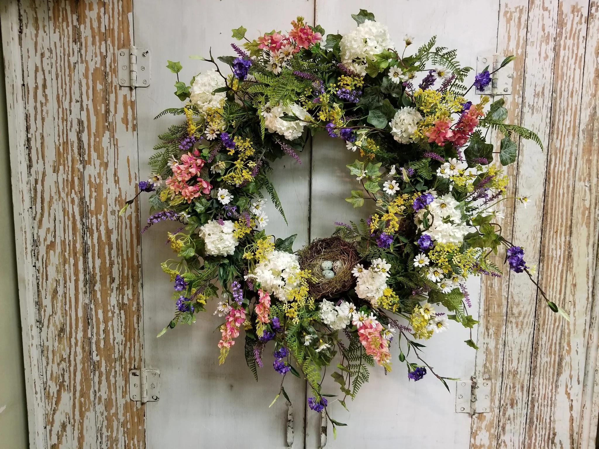 Ghirlanda primaverile fai da te con fiori rosa e bianchi appesa su una porta azzurra